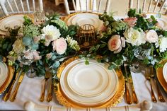 the table is set with white and gold plates, silverware, and floral centerpieces