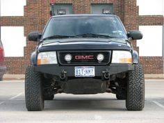 the front end of a black truck parked in a parking lot next to a brick building