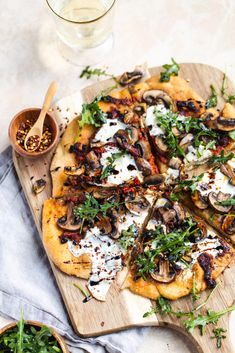 a pizza topped with mushrooms and cheese on a wooden cutting board next to two small bowls