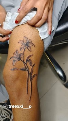 a woman's leg with a flower tattoo on the side of her thigh, while sitting in a chair