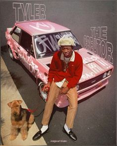 a man sitting on top of a pink car next to a brown dog and wearing a hat