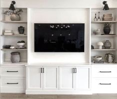 a white entertainment center with built in shelving unit and black screen television mounted on the wall