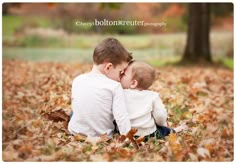 two young boys sitting in the leaves with their heads on each other's shoulders