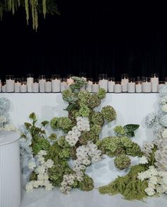 flowers and candles are arranged on the floor in front of a white wall with black curtains