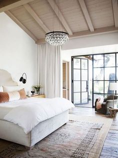 a large white bed sitting in a bedroom under a chandelier next to a sliding glass door