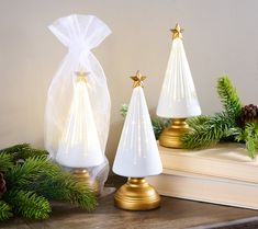 three white christmas trees with gold stars on them sitting on a shelf next to evergreen branches