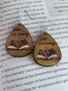 two wooden tear shaped earrings with flowers and an open book on the bottom, reading i'm reading