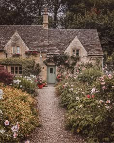 a stone house surrounded by lots of flowers and greenery with a green door in the middle