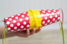 a hand holding a red and white polka dot tube wrapped in yellow paper with green streamers