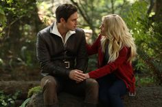 a man and woman sitting on a rock in the woods looking into each other's eyes