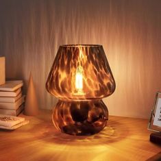 a lamp sitting on top of a wooden table next to a stack of books and an alarm clock