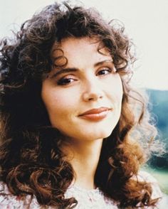 a close up of a woman with curly hair and blue eyes wearing a white shirt