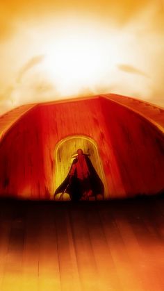 a person sitting on the ground in front of a red structure with an orange sky behind them