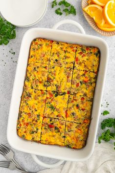 a casserole dish filled with meat and vegetables next to an orange slice on a plate