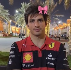 a man wearing a red and black shirt with a pink bow on his head in front of palm trees