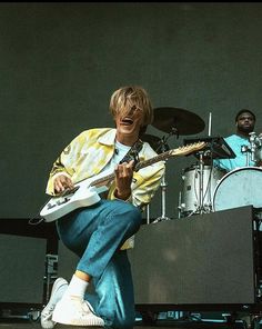 a man playing an electric guitar on stage with another man in the background behind him