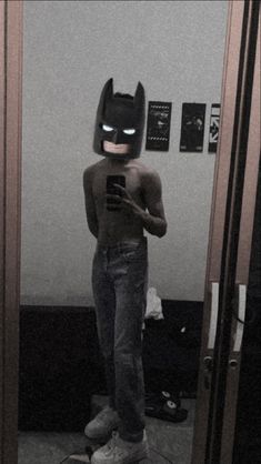 a person wearing a batman mask standing in front of a mirror with his cell phone