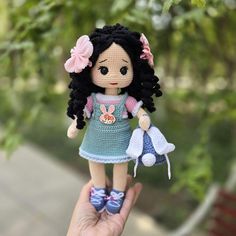 a hand holding a small doll in front of a tree