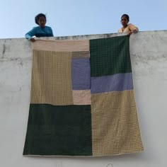 two people standing on a ledge with a large quilt