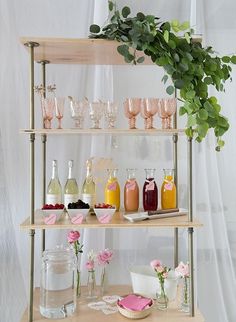 an assortment of drinks and condiments are displayed on a wooden shelf with greenery