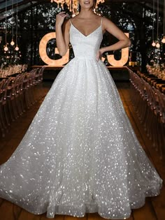 a woman in a white dress standing on a wooden floor with chandeliers hanging from the ceiling