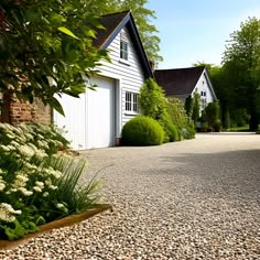 a driveway with gravel and plants next to a white house