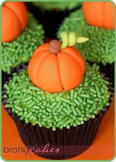 cupcakes decorated with green and orange frosting on an orange tablecloth are arranged in the shape of pumpkins