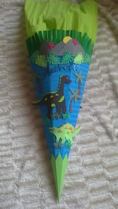 a green and blue paper cone shaped like a pyramid with dinosaurs on it, sitting on a bed