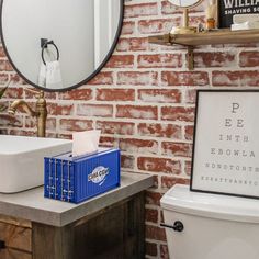 a bathroom with red brick walls and a white toilet next to a blue box on the counter