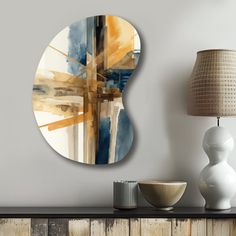 an abstract painting on the wall next to a lamp and table with a white vase