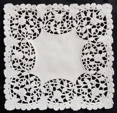 a white doily with an intricate design on the edges and center, in front of a black background