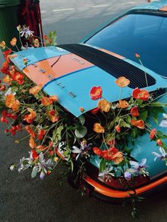 an orange and blue surfboard sitting on top of a car with flowers growing out of it