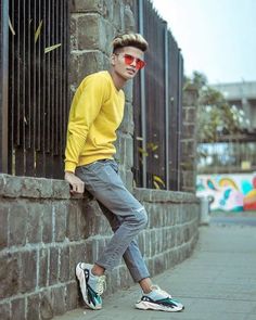 a young man leaning against a brick wall with his foot on the ground and wearing sunglasses