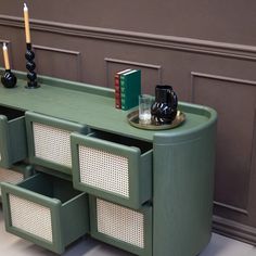 a green table with baskets and candles on it in front of a brown wall next to a book shelf