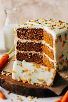 a carrot cake with white frosting and sprinkles on a wooden cutting board