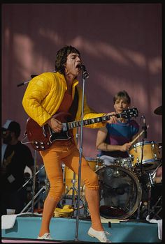 an image of a man that is on stage with a guitar and another person in the background