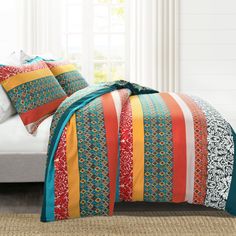 a bed with colorful comforters and pillows on top of it in front of a window