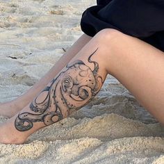 an octopus tattoo on the leg of a woman sitting in the sand at the beach