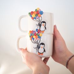 two mugs with penguins and balloons on them are being held by someone's hands