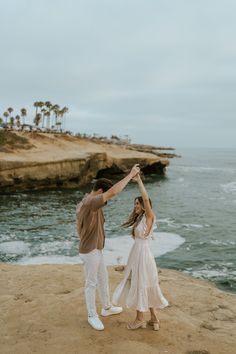 an engaged couple holding hands while standing on the beach with their arms in the air