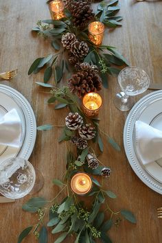 the table is set with pine cones, greenery and candles