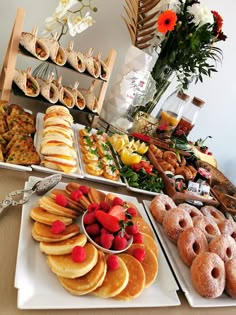 an assortment of pastries and desserts displayed on trays with flowers in the background