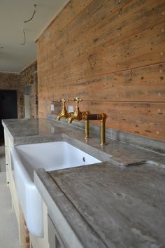 a kitchen counter with two faucets and a sink in front of a wooden wall