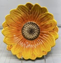 an orange and yellow flower shaped dish sitting on top of a metal stand in front of a white wall