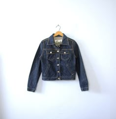 One vintage 1990's dark denim jacket, Express jean jacket, women's size small - Pointed collar. - 6 button closures going down the center front of the jacket. - 2 chest pockets with flaps and button closures. 2 slide pockets on the front of the jacket. - 1 button on each wrist cuff. - 2 tabs on the back of the waistband with 2 adjustable buttons. - Shorter, feminine fit through the torso. - Thick 100% cotton. Not broken in. - Color scheme: dark blue denim. Silver toned hardware. | CONDITION | A+ Vintage Dark Wash Button-up Denim Jacket, Retro Denim Blue Denim Jacket For Fall, Fitted Winter Denim Jacket, Fitted Denim Jacket For Winter, Dark Wash Cotton Denim Jacket With Buttons, Fitted Denim Jacket In Dark Wash With Button Closure, Fitted Dark Wash Denim Jacket With Button Closure, Fitted Denim Jacket With Button Closure In Dark Wash, Dark Wash Denim Jacket With Buttons