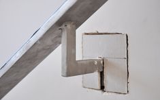 the corner of a white wall with a metal handrail attached to it, and a piece of wood sticking out from underneath