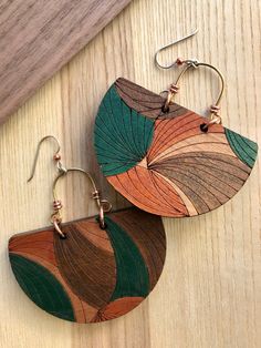 two wooden earrings with green, brown and orange designs on them sitting on top of a wooden table