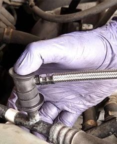 a person in purple gloves is working on an engine hose and connecting it to the car