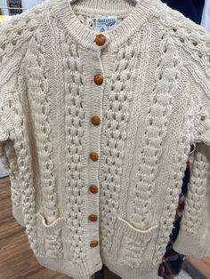 a white knitted sweater with buttons on the front and back, sitting on a wooden floor