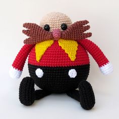 a crocheted stuffed animal is wearing a red and yellow hat with black eyes